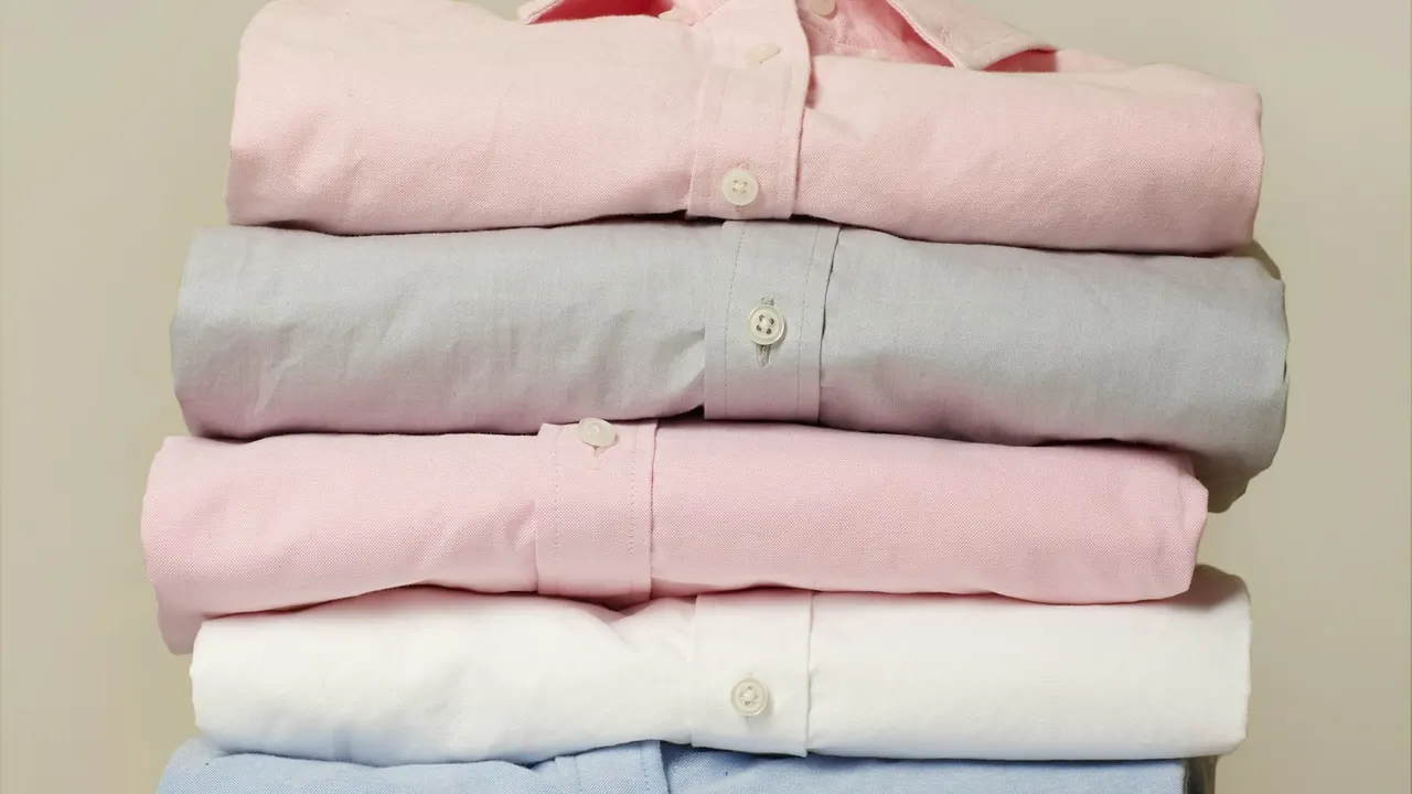Três peças de uniforme dobradas lado a lado: camiseta, polo e camisa social, na mesma cor