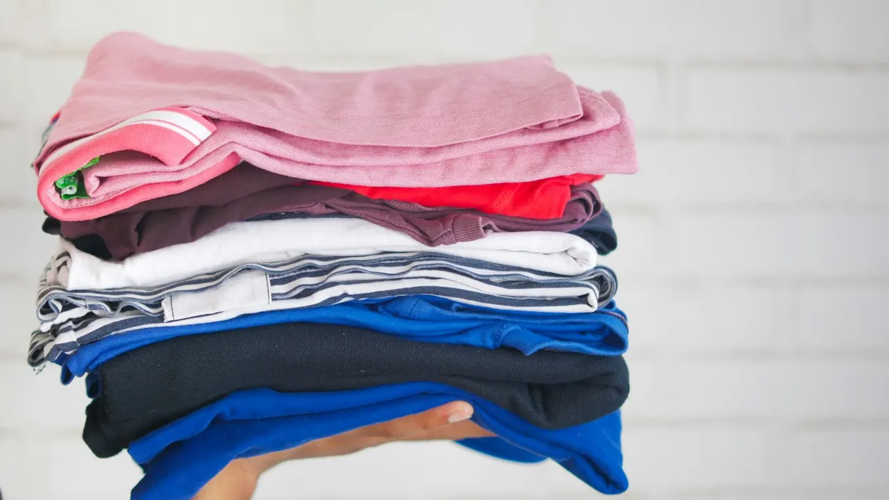 Pilha de camisetas dobradas em várias cores, prontas para uniforme escolar