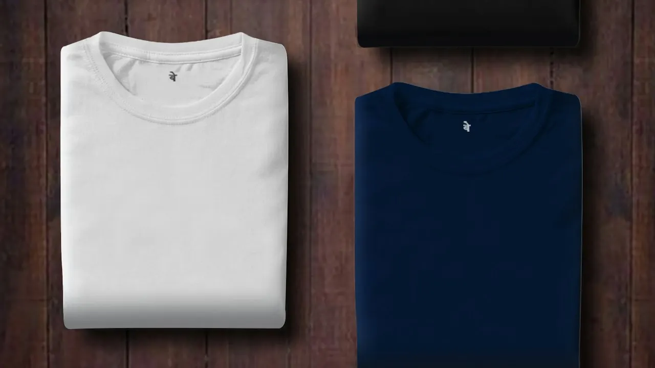 Camisetas dobradas nas cores branca e azul-marinho sobre uma mesa de madeira